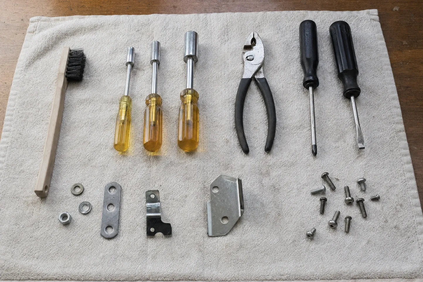 Nut drivers, screwdrivers, pliers and a wire brush laid out with three steel mounting brackets and a scatter of machine screws
